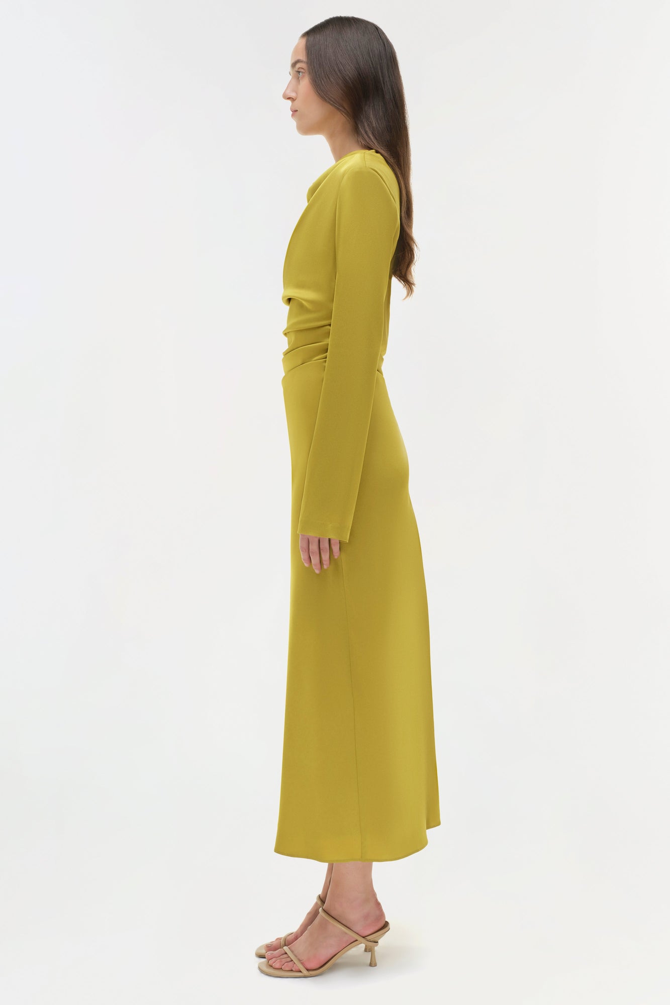 Woman wearing a yellow-green satin midi dress with long sleeves, shown in profile view.