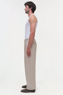 Man wearing beige textured Duncan pants with white tank top, shown in profile view.