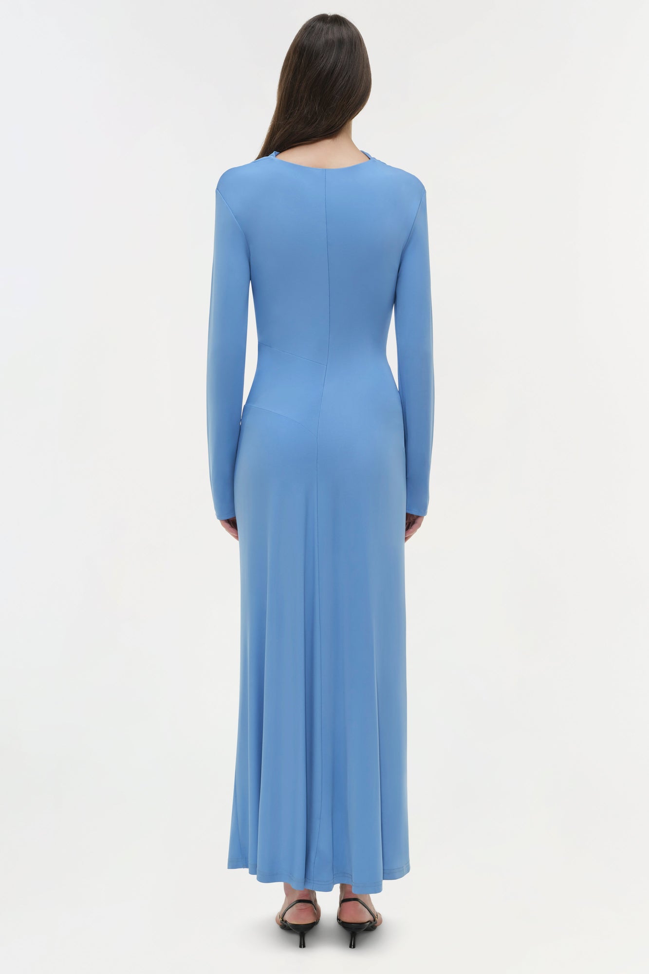 Woman wearing a blue draped jersey midi dress with long sleeves, shown from back view.