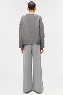 Gray knit sweater with floral embellishments on sleeves, worn with light gray wide-leg pants, back view.