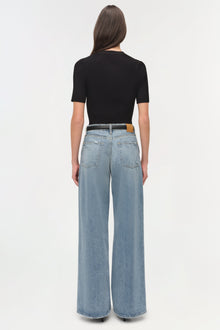 Light blue straight-leg denim crop pants with brown leather patch, shown from back view on model wearing black ribbed top.