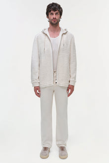 Man wearing cream hooded zip-up jacket over white ribbed shirt with cream pants and sneakers.
