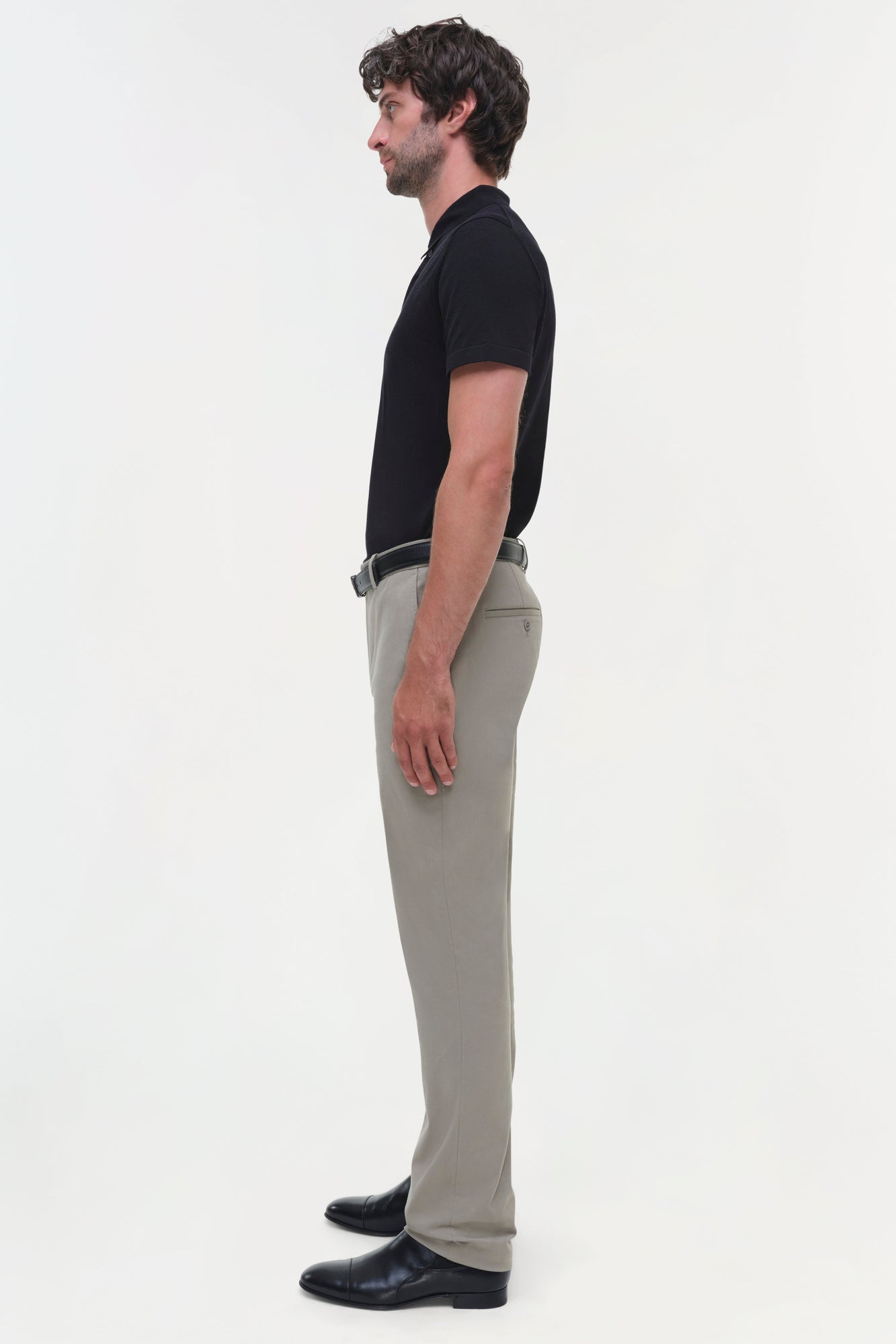 Man wearing beige cotton twill trousers with black shirt and belt, shown in side profile.