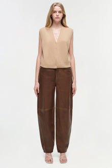 Brown leather pants with curved legs and relaxed fit, styled with beige sleeveless vest.