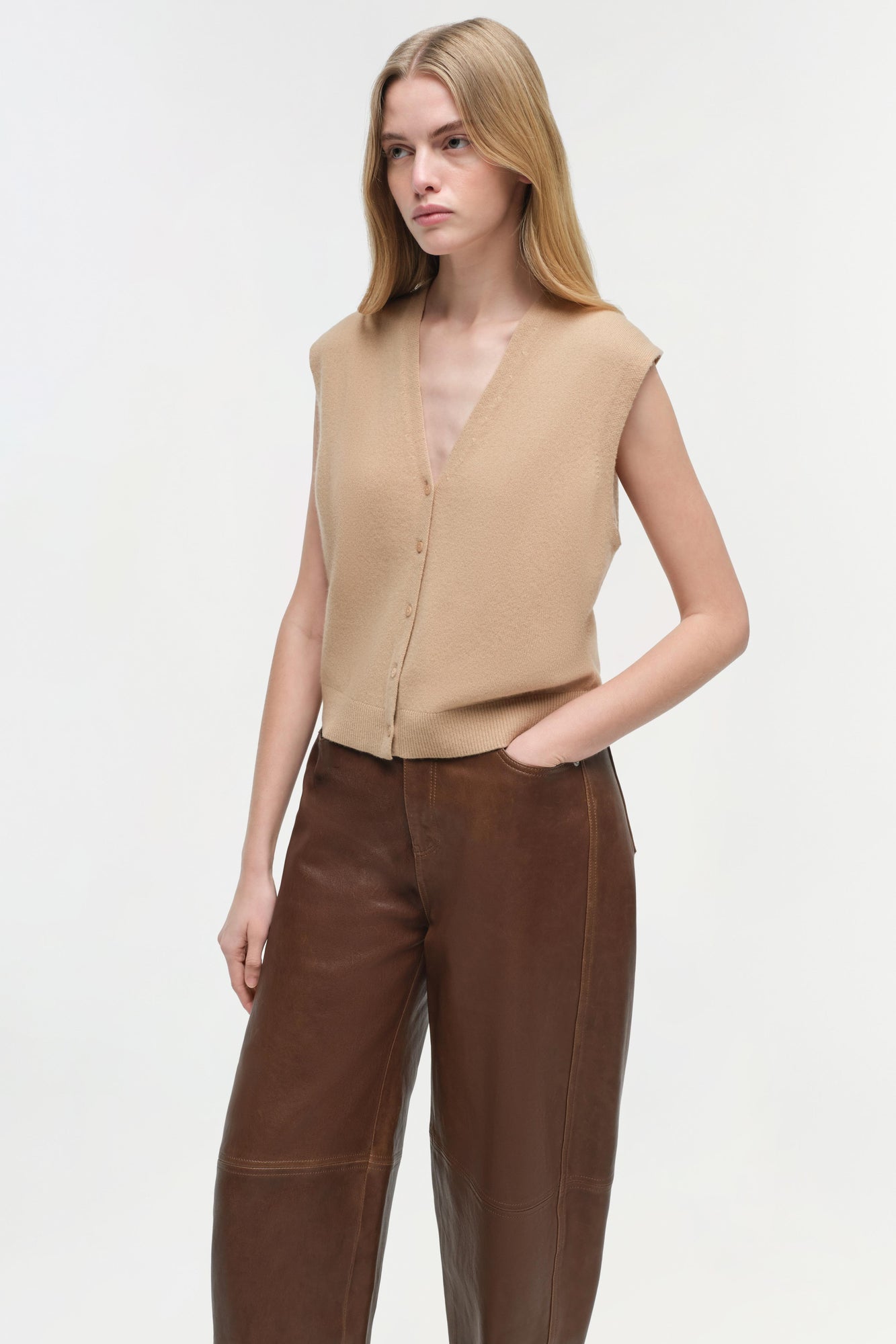 Woman wearing beige sleeveless button-front vest and brown leather pants with curved legs.