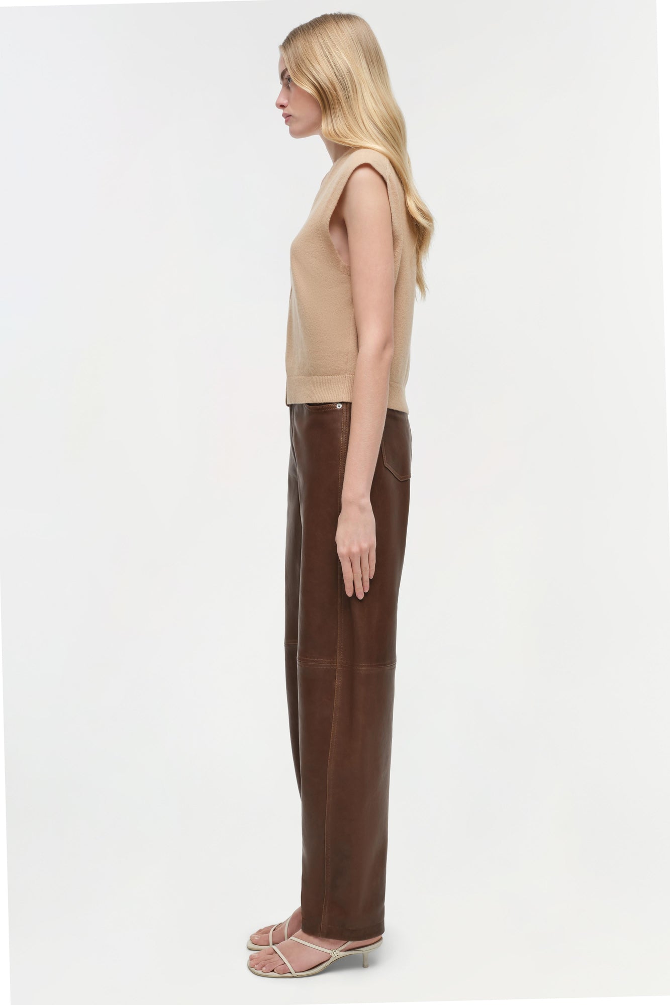 Beige sleeveless cashmere vest on model wearing brown leather pants and strappy heels.