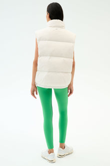 Wearing the SPLITS59 Summit Nylon Puffer Vest in white, paired with bright green leggings and white sneakers, a person stands facing awayâ€”showcasing a lightweight, stylish option for cool weather workouts against a plain background.