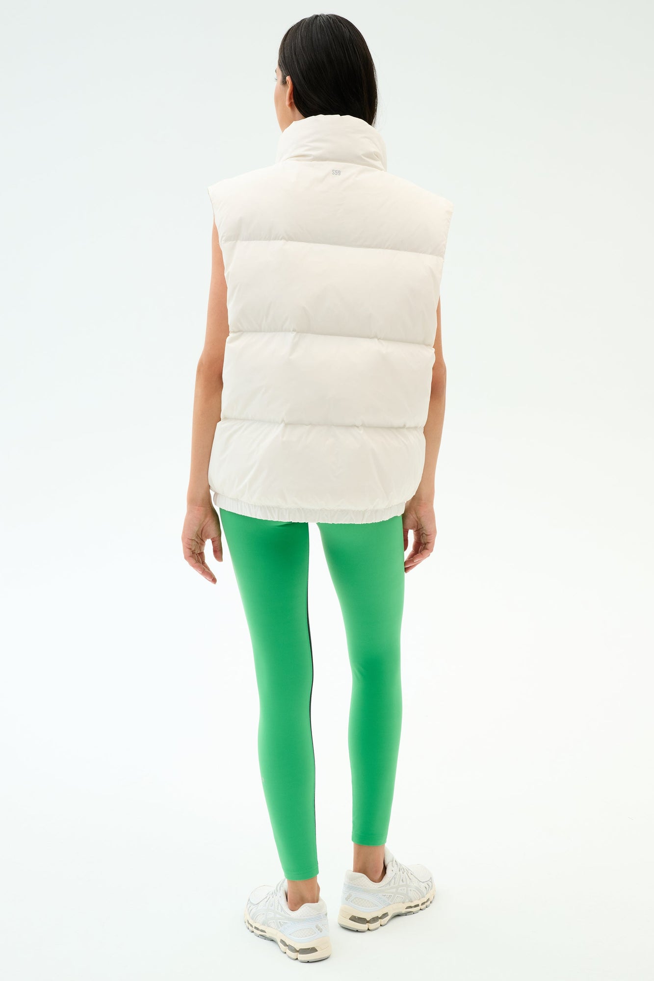 Wearing the SPLITS59 Summit Nylon Puffer Vest in white, paired with bright green leggings and white sneakers, a person stands facing awayâ€”showcasing a lightweight, stylish option for cool weather workouts against a plain background.