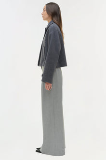 Woman wearing charcoal wool jacket with notch collar over light gray wide-leg trousers, shown in profile view.