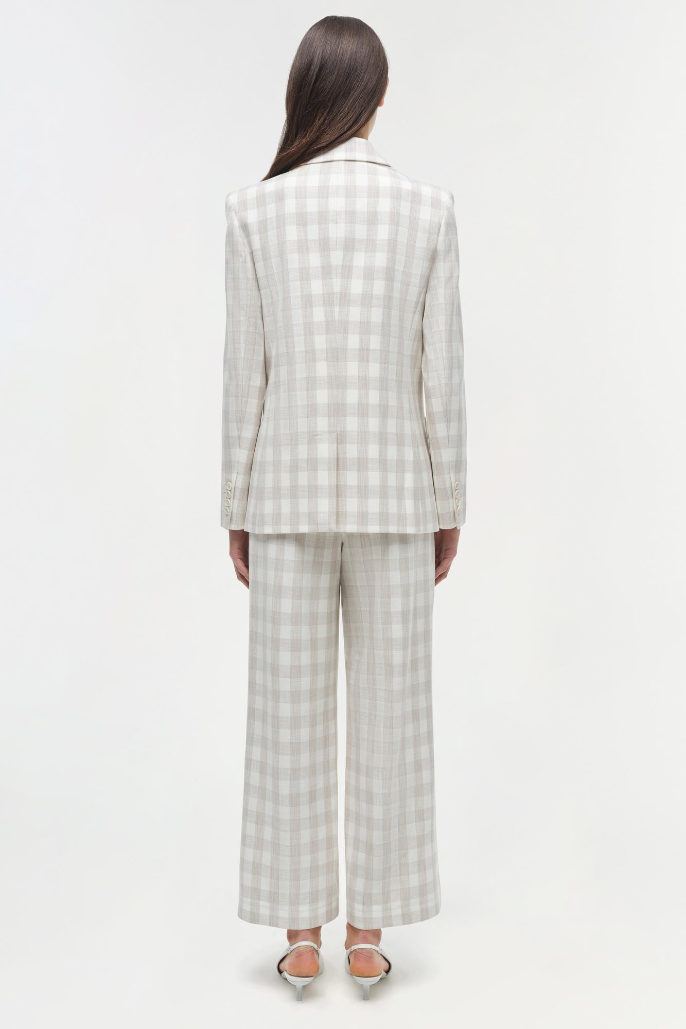 Woman wearing a cream and white gingham double breasted blazer with matching wide-leg trousers, shown from back.