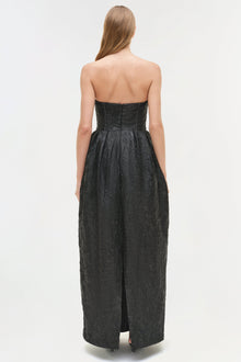 Black jacquard bustier gown with strapless neckline and floor-length skirt with side slit, back view.