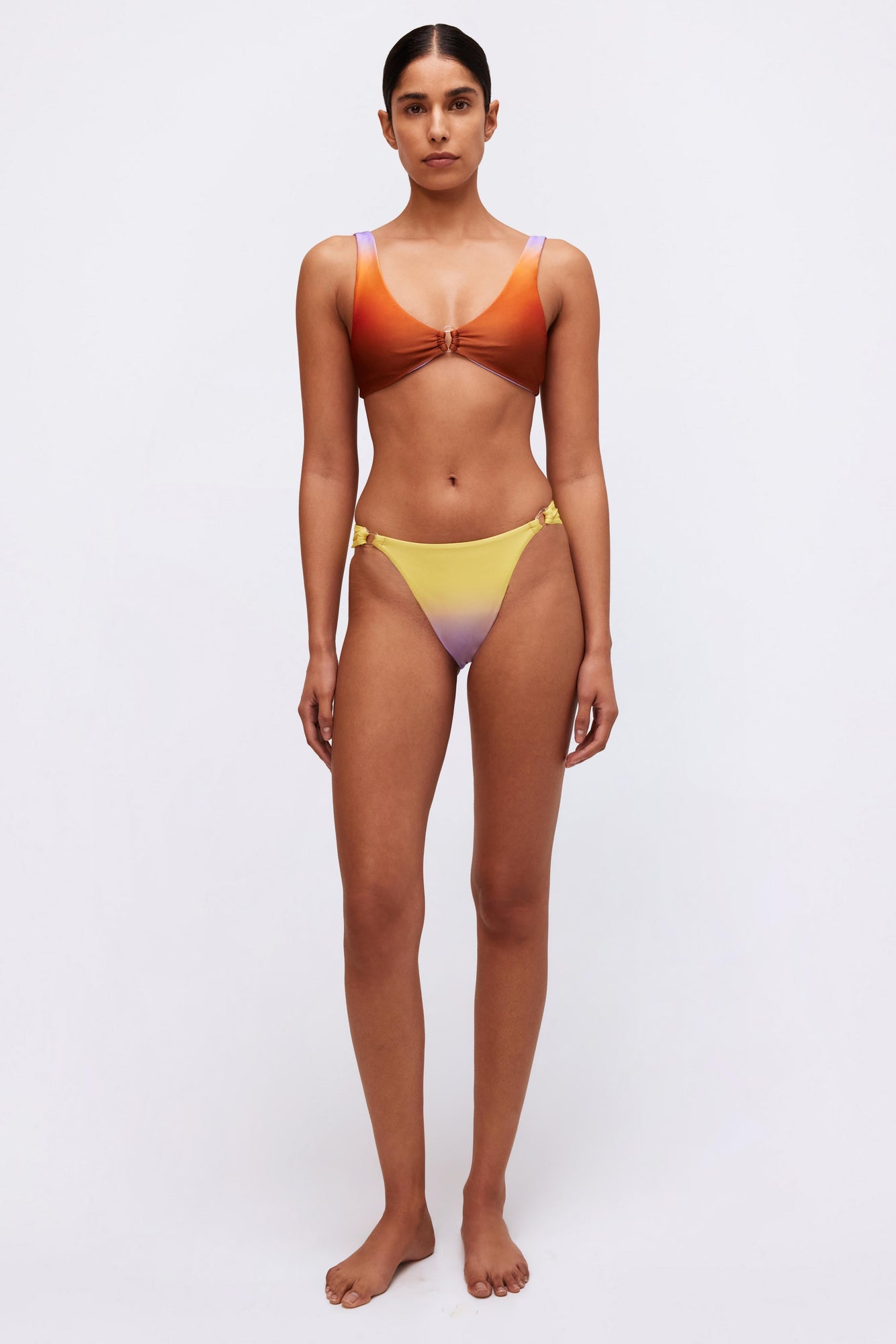 Yellow and purple ombre bikini bottom with side ring details on a model.