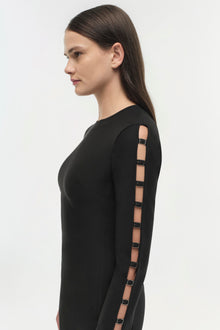 Black long-sleeve dress with cutout side panel and metal buckle details shown on model in profile view.