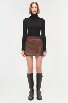 Brown leather mini skirt with side snap closure styled with black turtleneck and black boots.