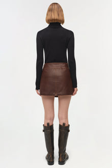 Brown leather mini skirt with front seam detail, worn with black turtleneck and dark boots, back view.