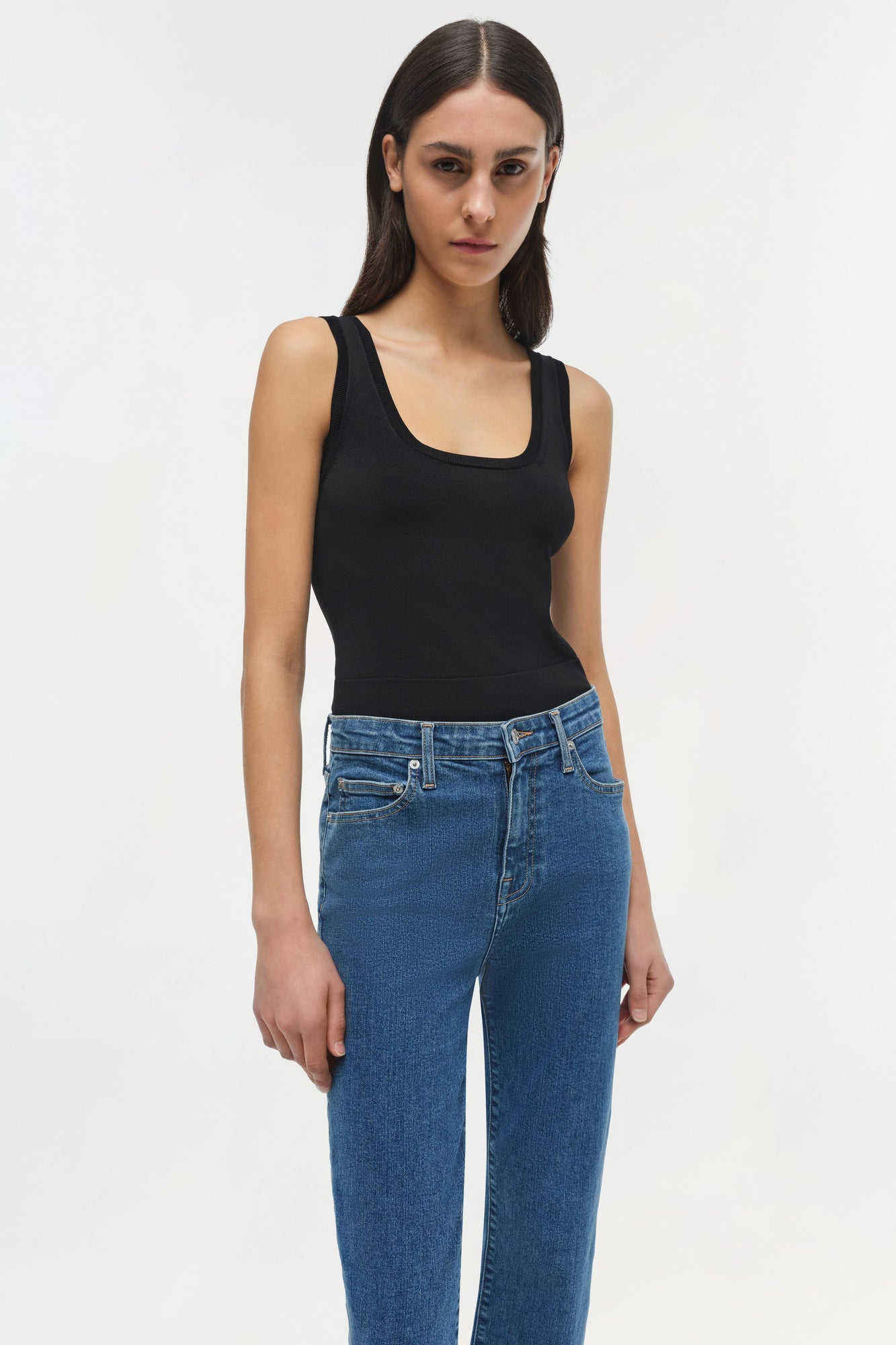 Woman wearing black sleeveless tank top and blue straight-leg jeans with classic five-pocket styling.