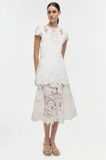 White lace dress with short sleeves, decorative cutout patterns, and asymmetrical tiered skirt.