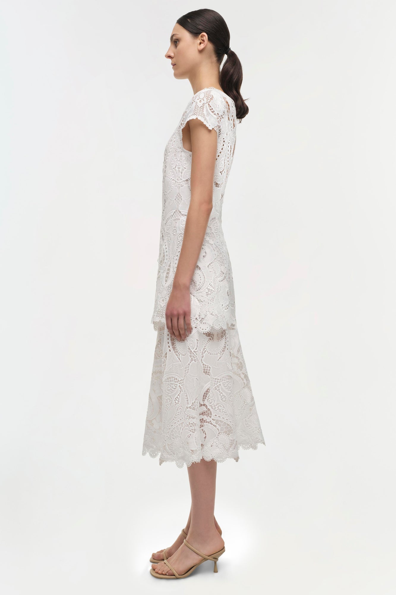 White lace midi dress with short cap sleeves and scalloped hem, shown on model in profile view.