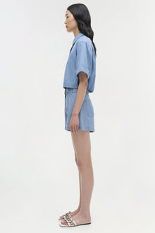 Light blue denim bishop top with puffed sleeves worn with matching denim shorts.