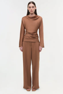 Woman wearing camel-colored satin wide-leg pants with a matching long-sleeve cowl neck top.
