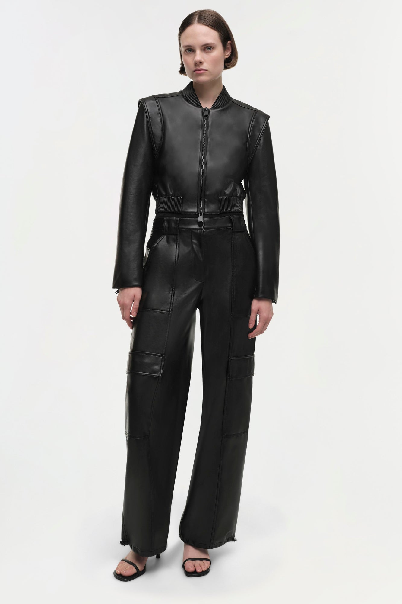 Woman wearing black leather cropped jacket with ribbed collar and cuffs, paired with matching cargo pants.
