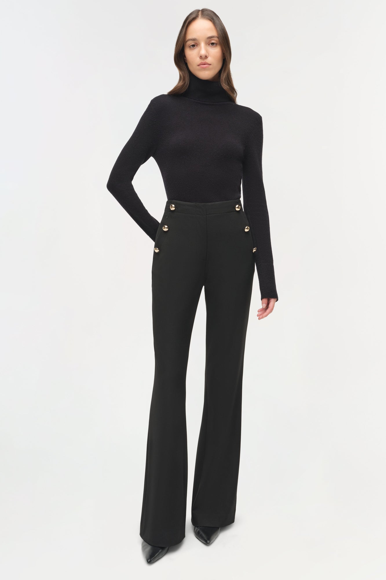 Black tailored trouser with gold button details at waistband, paired with black turtleneck sweater.