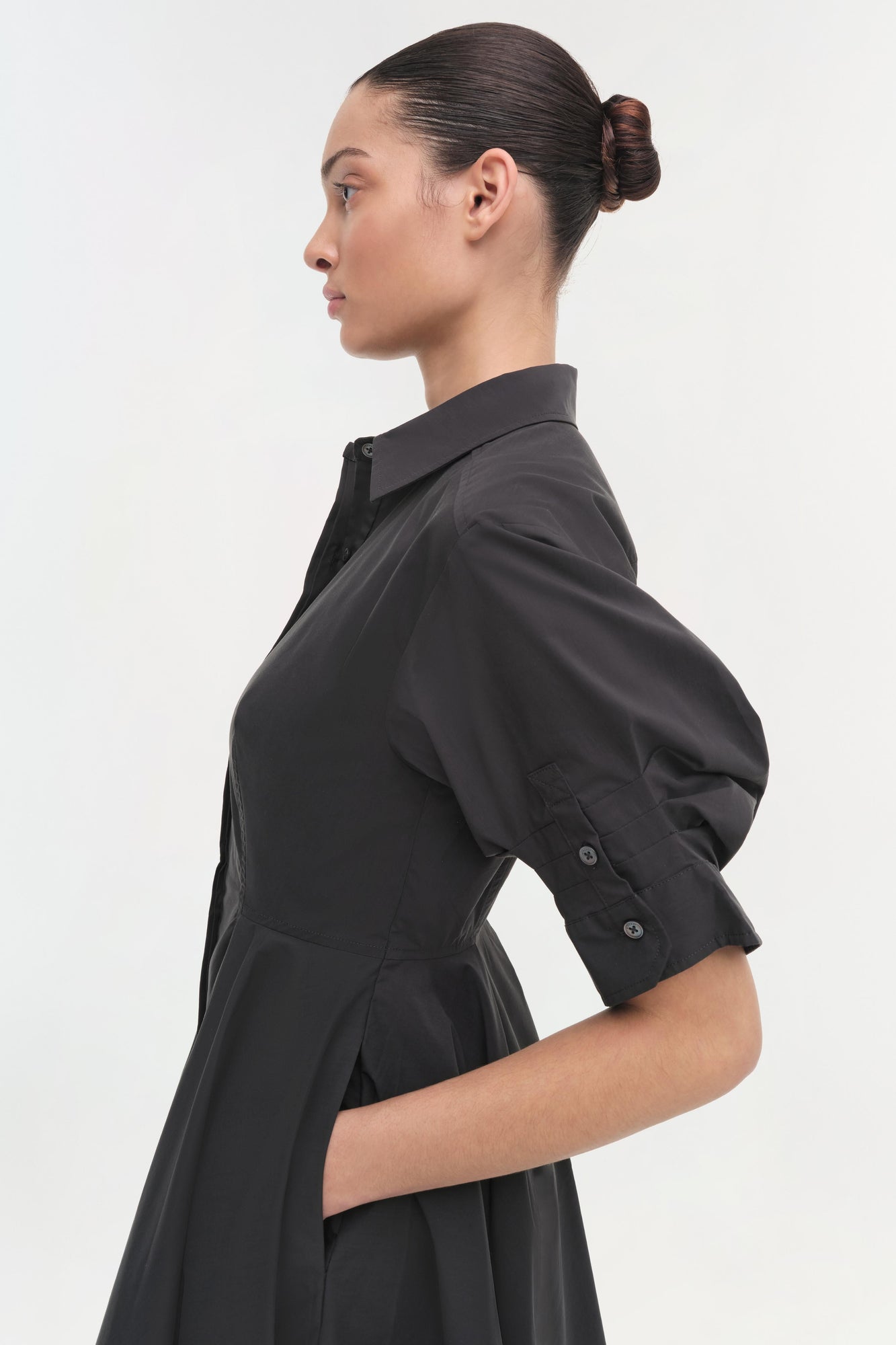 Black collared shirt dress with half sleeves and button front closure, shown on model in profile view.