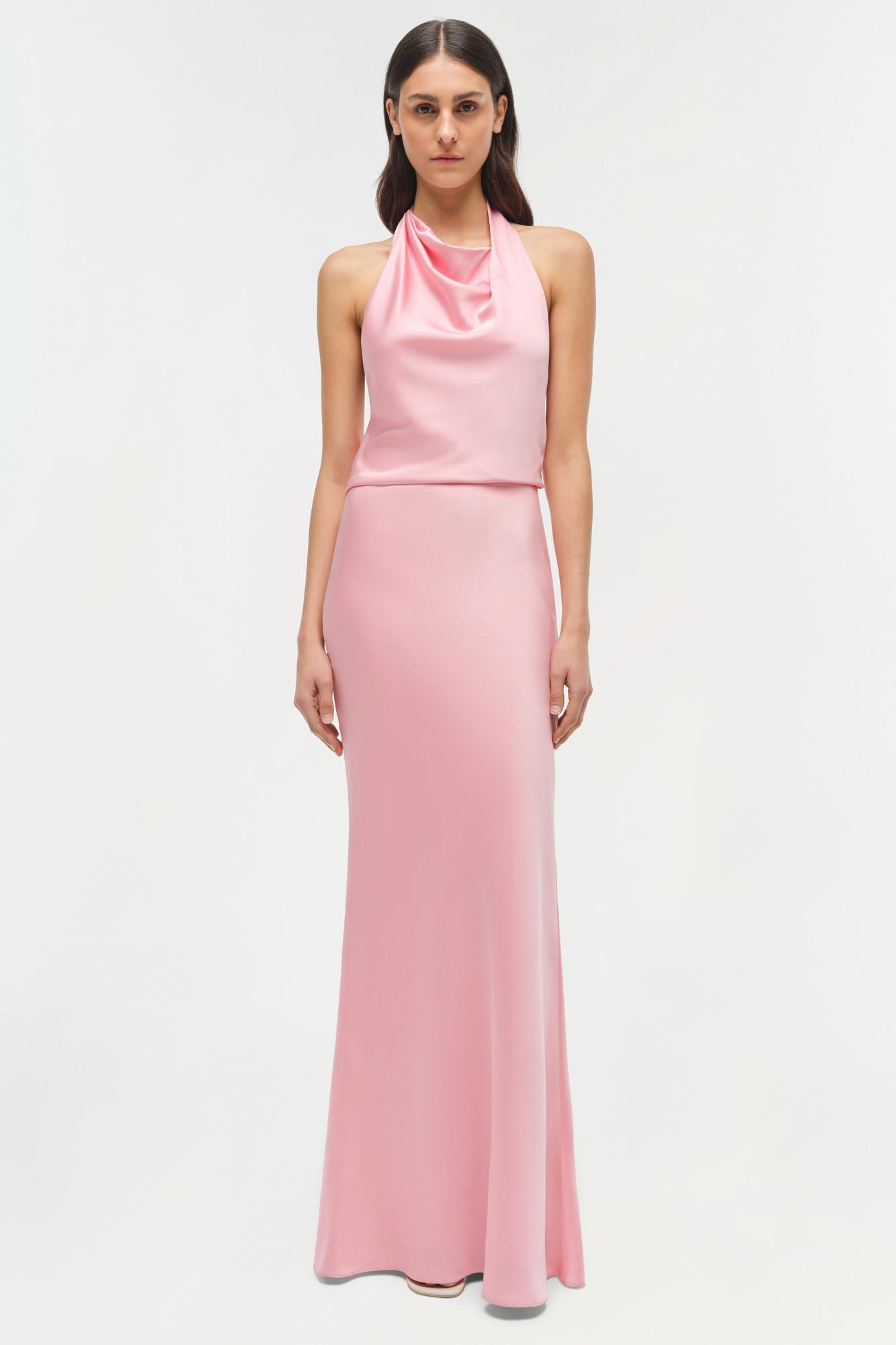 Woman wearing a pink sleeveless halter gown with draped neckline and fitted silhouette.