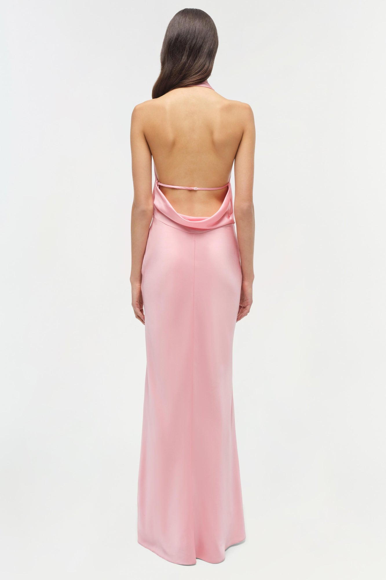 Woman wearing a pink satin gown with an open back and draped neckline, shown from behind.