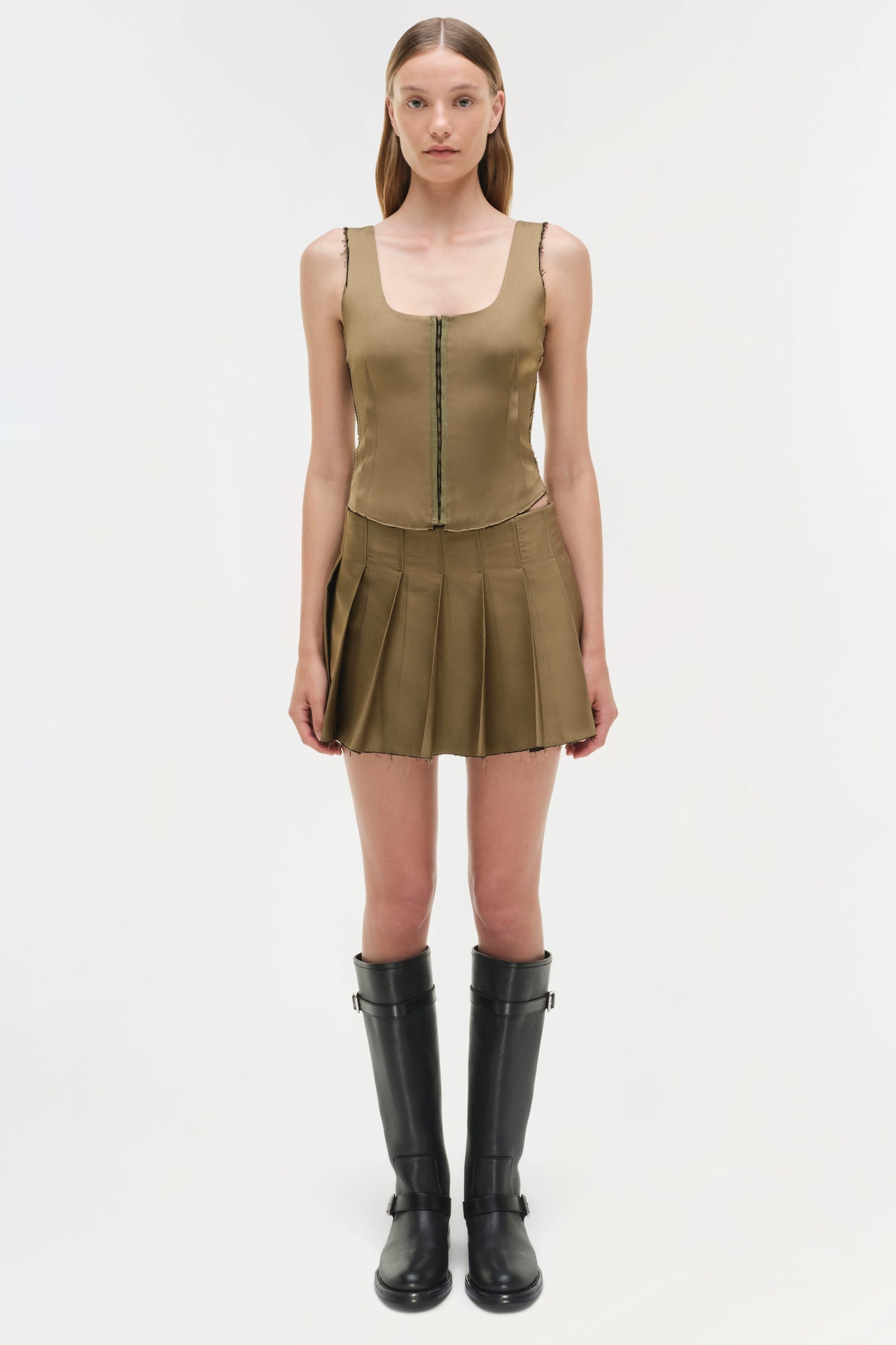 Khaki sleeveless bustier top with front zip closure and pleated skirt bottom, styled with black knee-high boots.