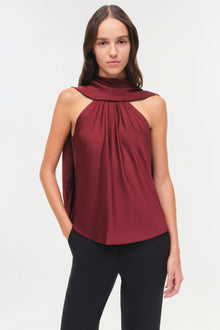 Burgundy sleeveless halter top with draped cape detail and gathered front, worn with black pants.