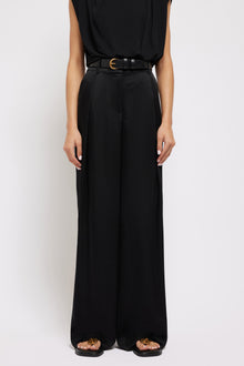 Black wide-leg pants with pleated front, gold buckle belt, and full-length straight silhouette.