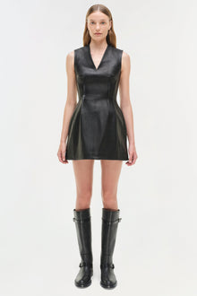 Black leather sleeveless mini dress with V-neckline and seamed bodice, styled with black knee-high boots.