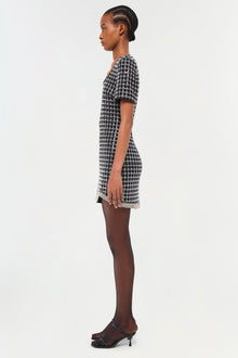 Black and white houndstooth mini dress with short sleeves and lace trim hem, shown on model in profile view.