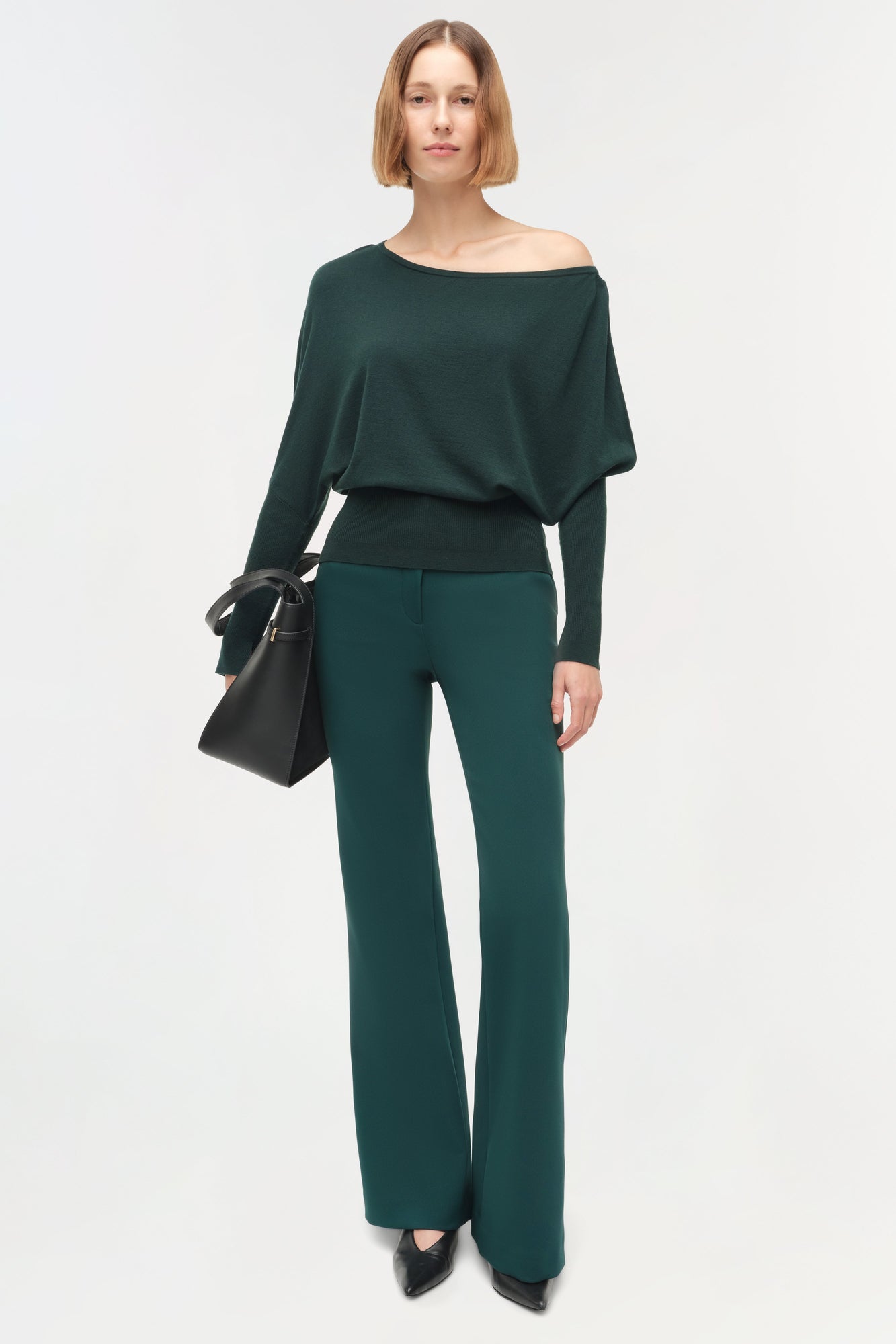 Dark green off-shoulder sweater with draped sleeves worn with matching wide-leg pants.