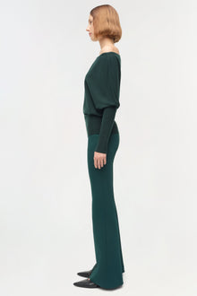 Woman wearing a dark green off-shoulder sweater with matching wide-leg pants, shown in profile view.