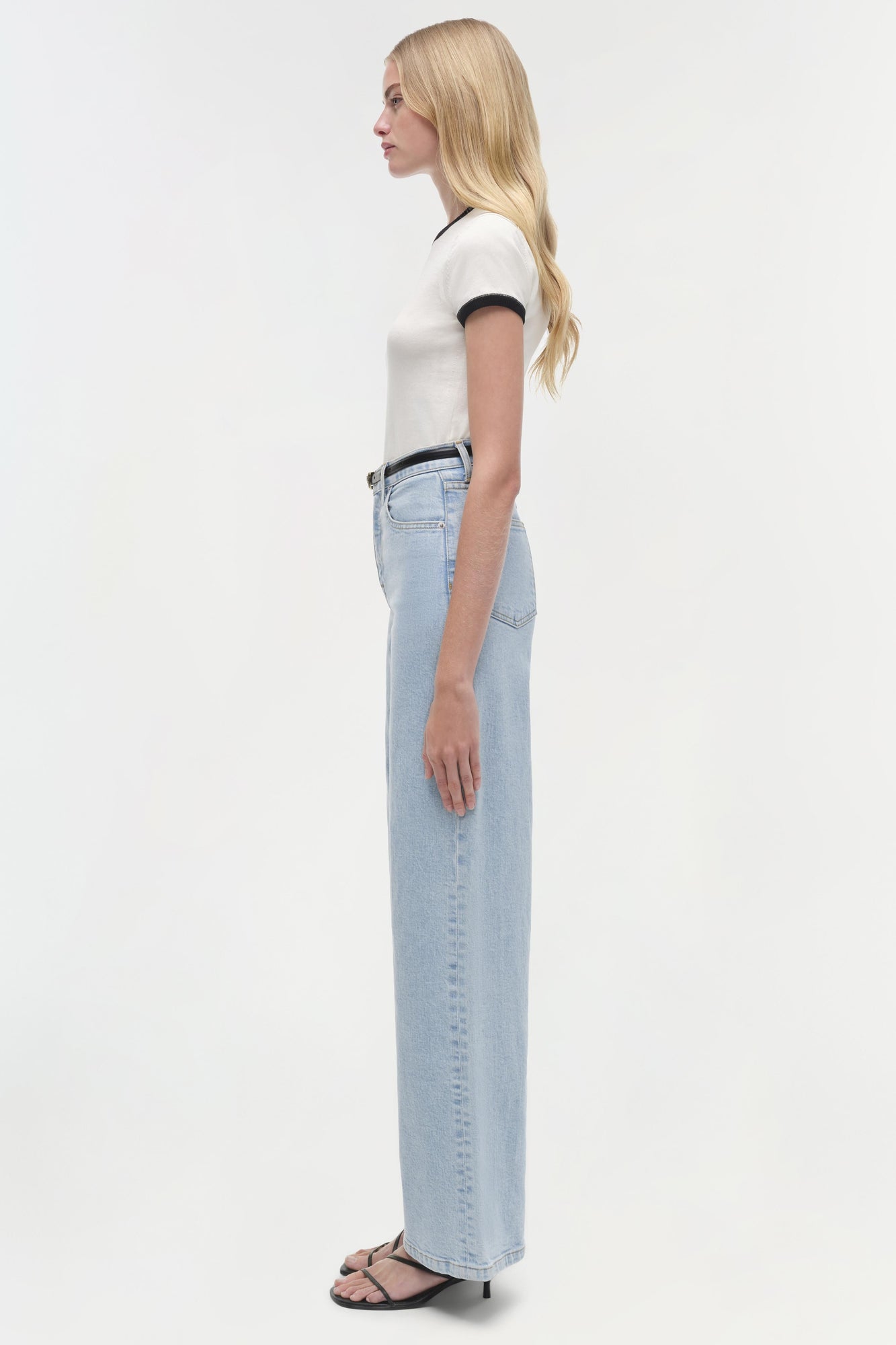 Woman wearing white short-sleeve top with navy trim and light blue straight-leg jeans, shown from the side.
