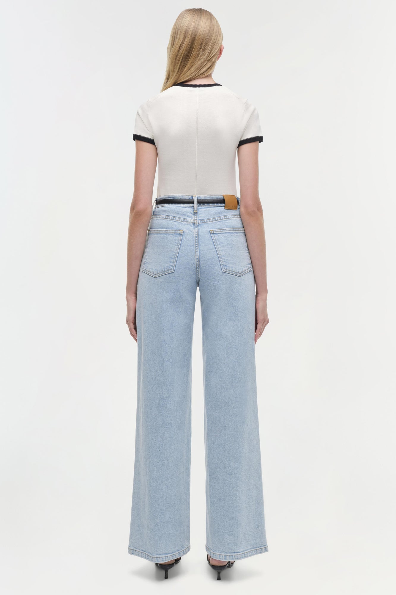 Woman wearing cream short-sleeve top with black trim and light blue jeans, shown from back view.