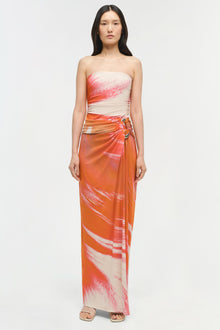 Woman wearing strapless jersey gown with cream, coral, and orange watercolor pattern and ruched waist detail.
