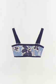 Blue bikini top with navy floral print, dark trim, and adjustable shoulder straps with metal hardware.