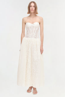 Woman wearing ivory strapless dress with lace corset bodice and full lace skirt, paired with white sandals.