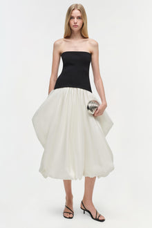 Strapless midi dress with black fitted bodice and cream pleated skirt, worn with black strappy heels.