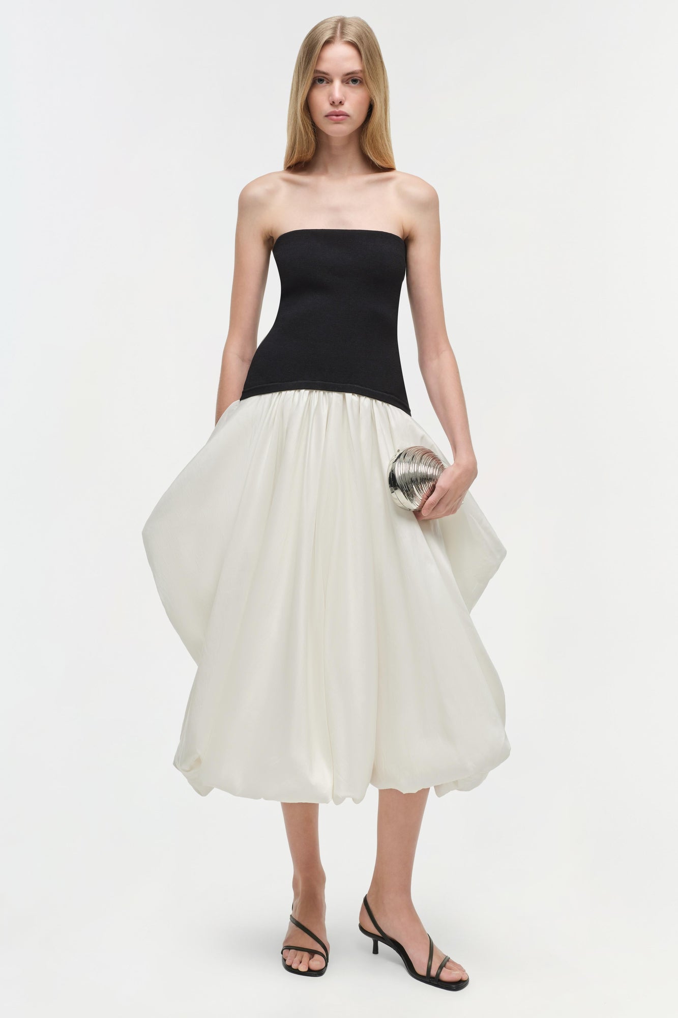 Strapless midi dress with black fitted bodice and cream pleated skirt, worn with black strappy heels.