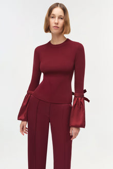 Burgundy ribbed knit top with taffeta bell sleeves and bow cuffs on a model.