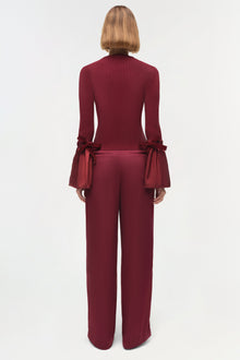 Burgundy knit top with flared sleeves featuring bow ties at the cuffs, shown on model from back view.