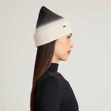Woman wearing a black and white ombre beanie on a light gray background