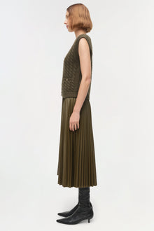 Olive green cable-knit cashmere vest with ribbed trim worn over pleated skirt.
