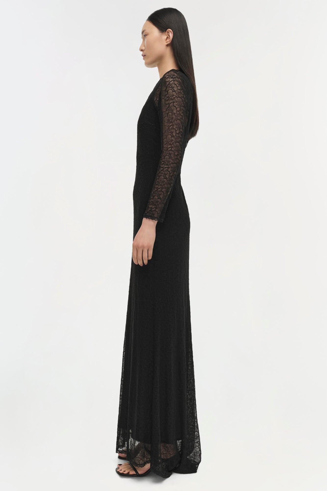 Black long-sleeve lace gown with floor-length skirt and lace sleeves, shown from side profile.
