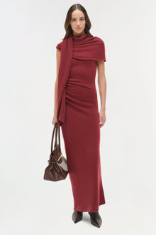 Burgundy midi dress with short sleeves, draped shoulder wrap, and matching scarf detail worn with brown leather handbag.