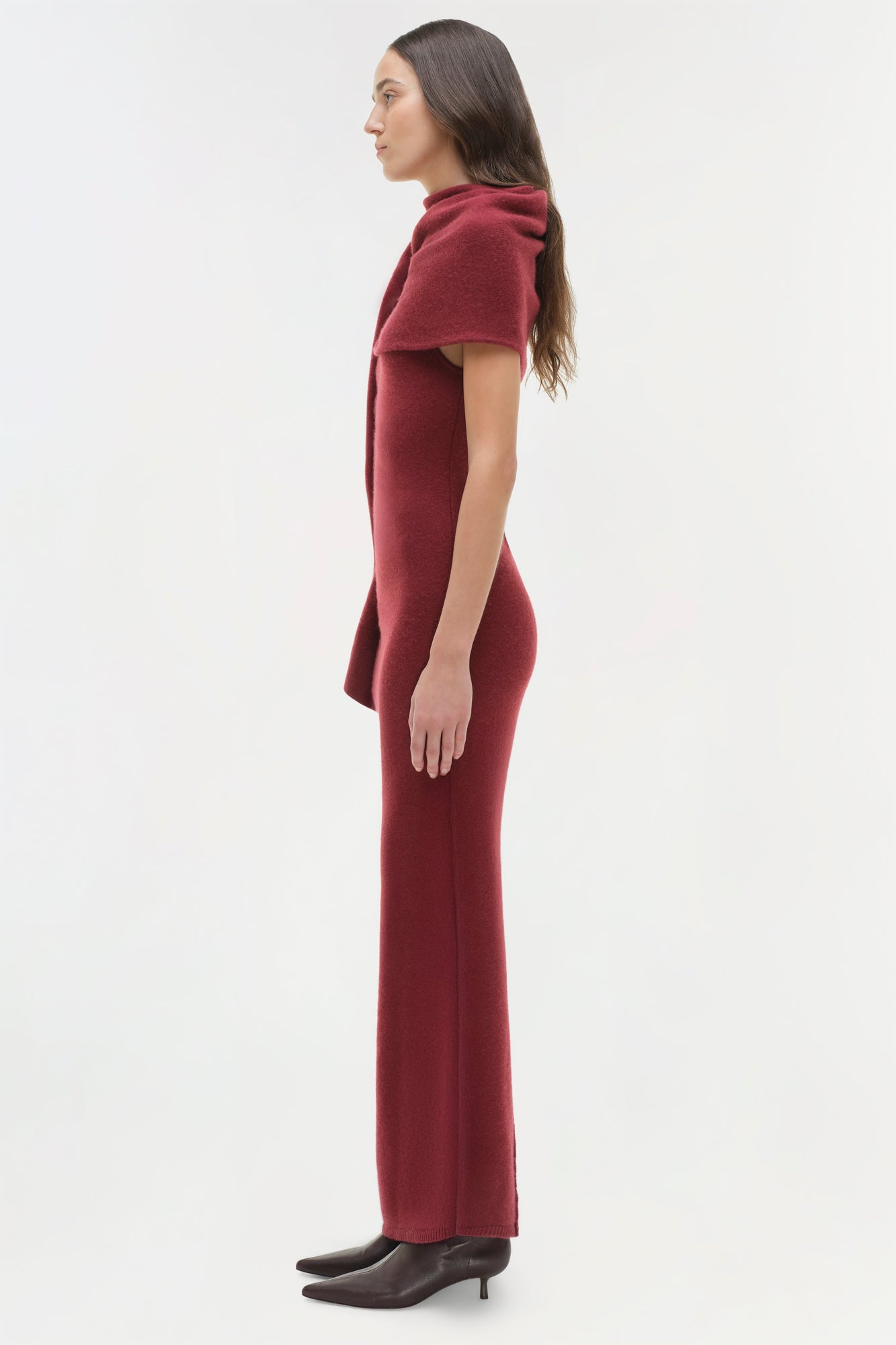 Woman wearing burgundy midi dress with draped shoulder detail and black kitten heels, shown in profile.